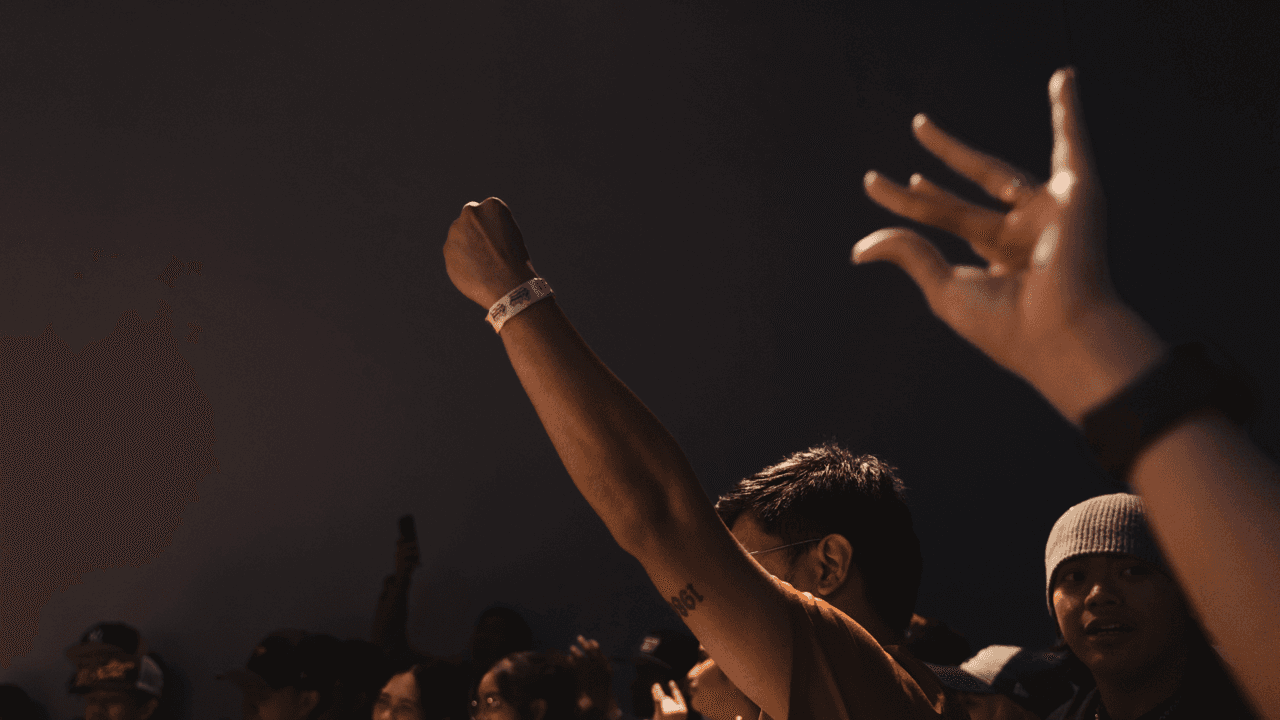 Raised fists and hands in a dimly lit crowd, dramatically backlit.