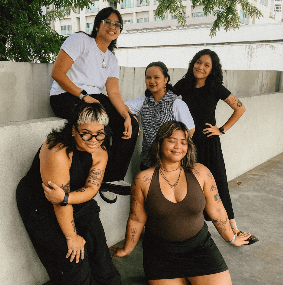 Five women posing playfully on and around a low wall, smiling for the camera.